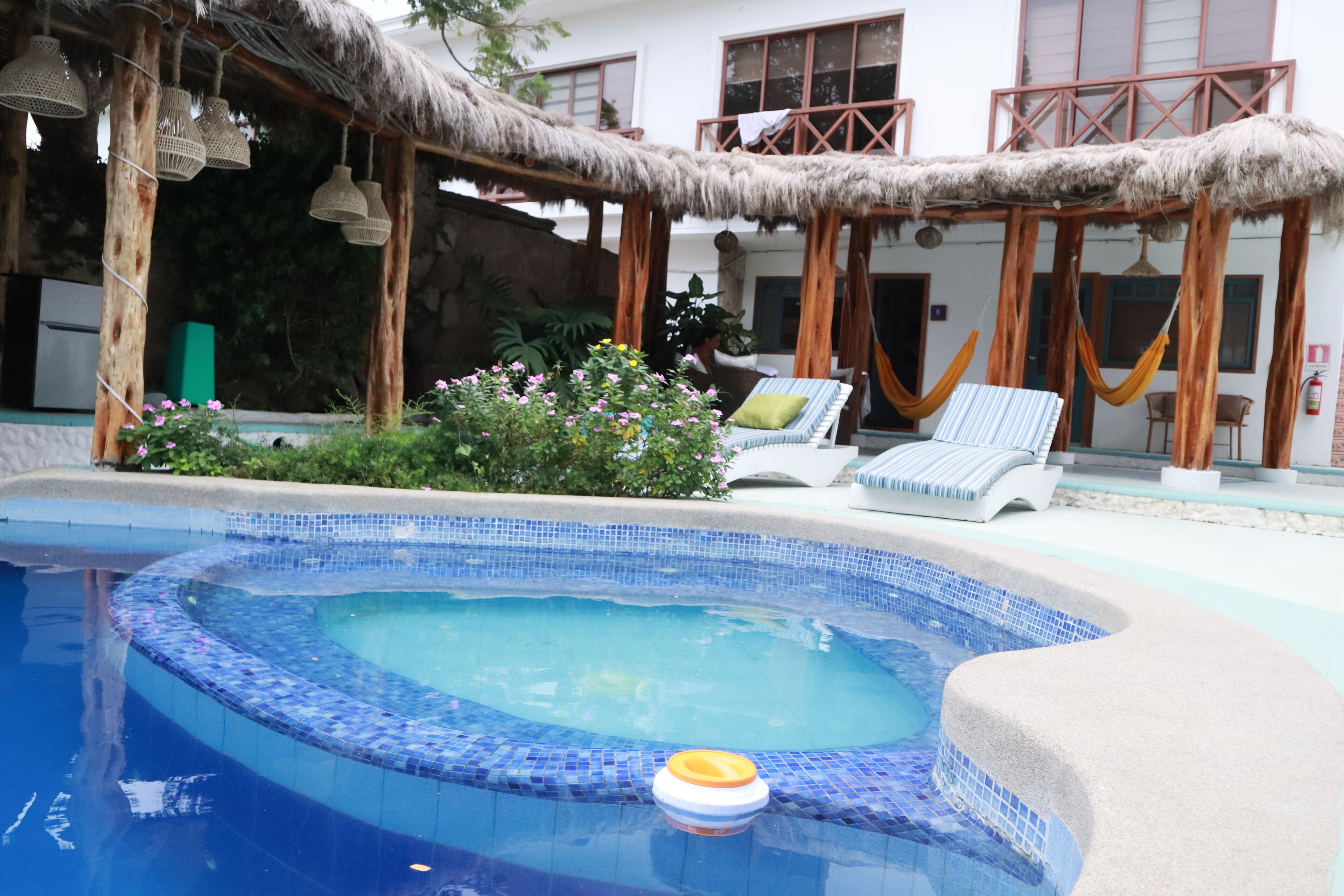 Una piscina con borde de azulejos, una silla de descanso y una estructura de techo de paja.