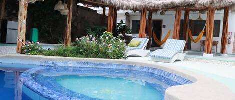 Una piscina con borde de azulejos, una silla de descanso y una estructura de techo de paja.