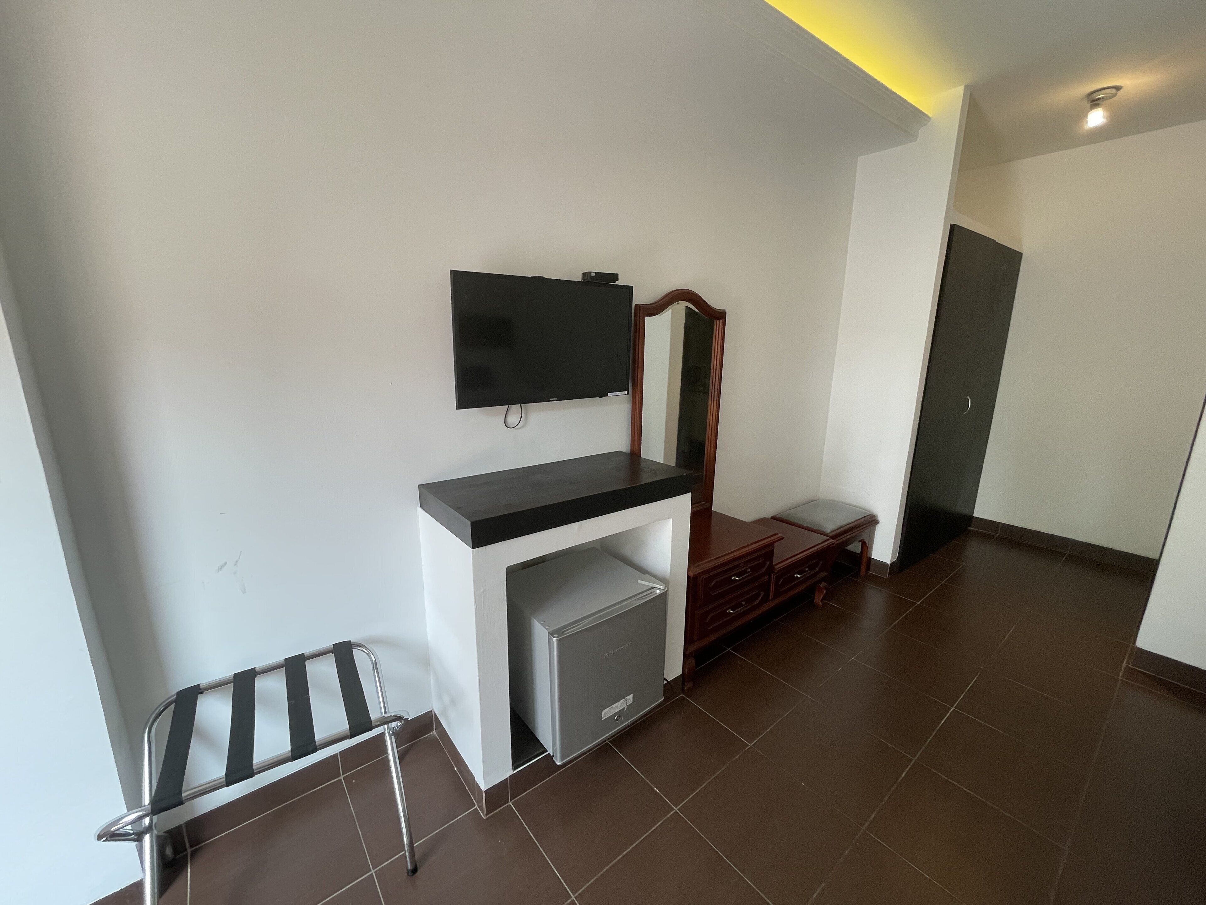 Een kamer met een flatscreen televisie aan de muur, een klein bankje en een houten kast.