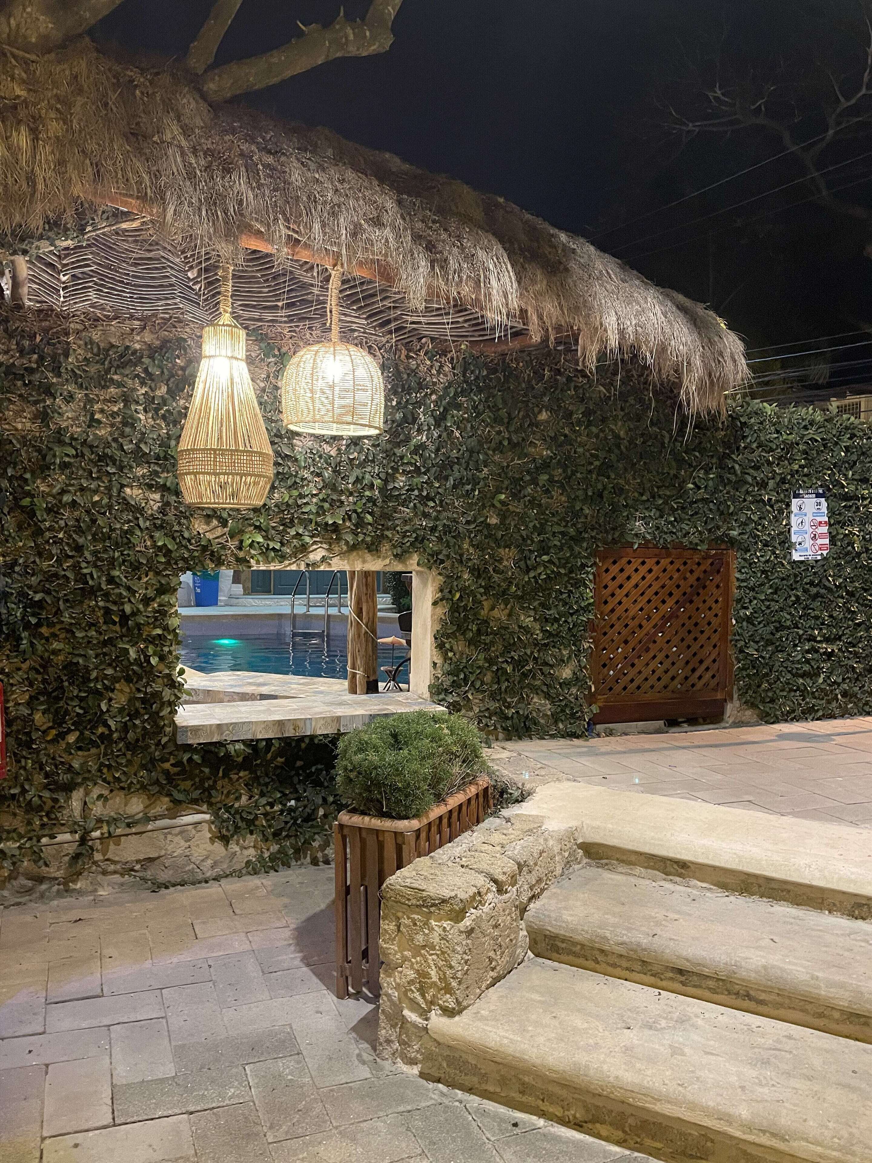 A thatched-roof structure with hanging wicker lamps, a window, and a wooden gate.