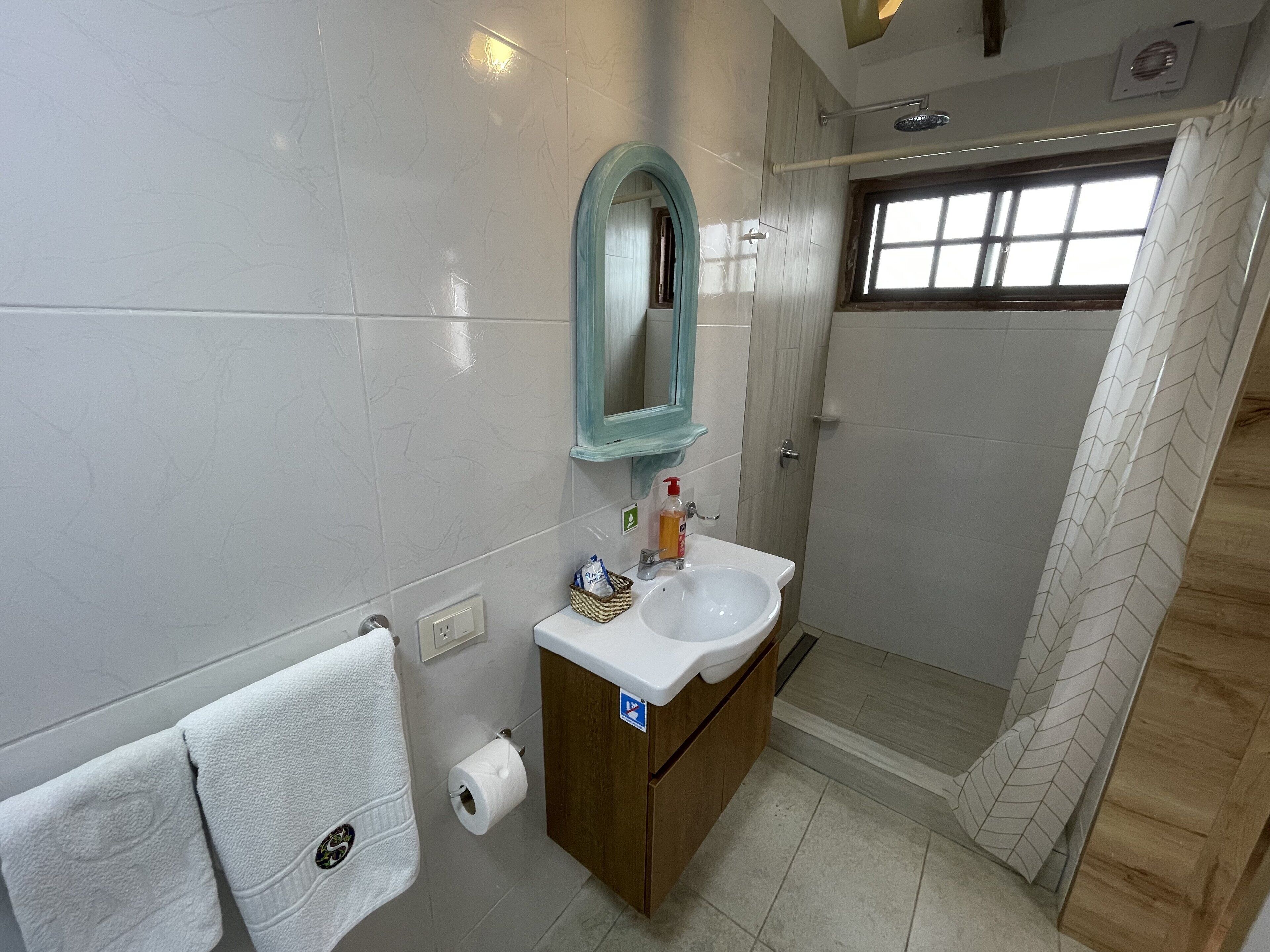 A bathroom with a white sink, a mirror, a towel rack, and a shower area.