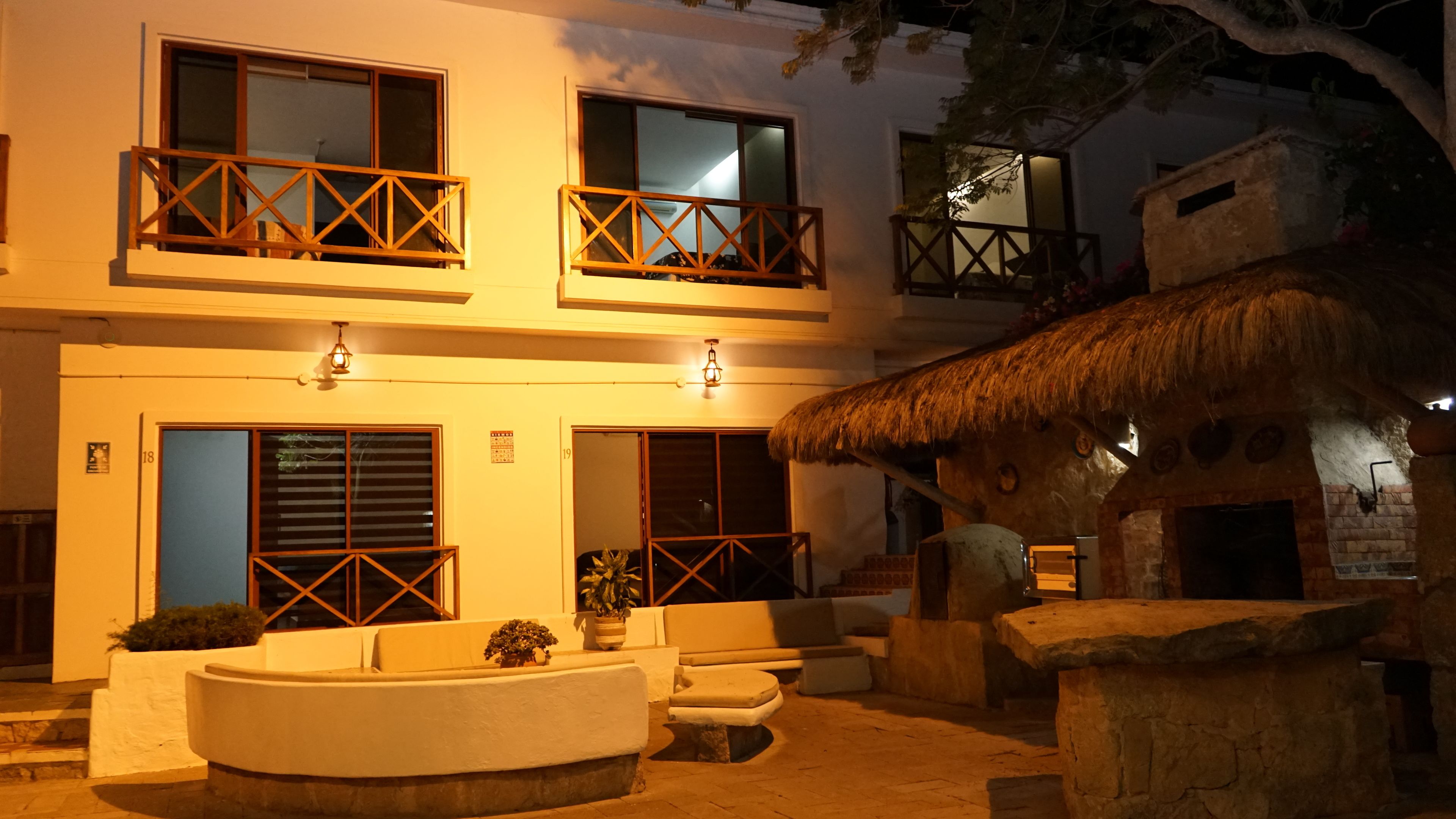 A two-story building with balconies, a thatched-roof structure, and a central seating area with a round table.