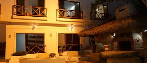 A two-story building with balconies, a thatched-roof structure, and a central seating area with a round table.
