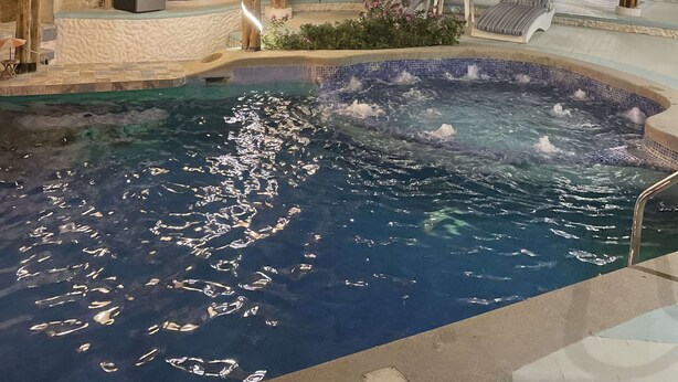 Un área de piscina con jacuzzi, sillones de descanso e iluminación colgante.