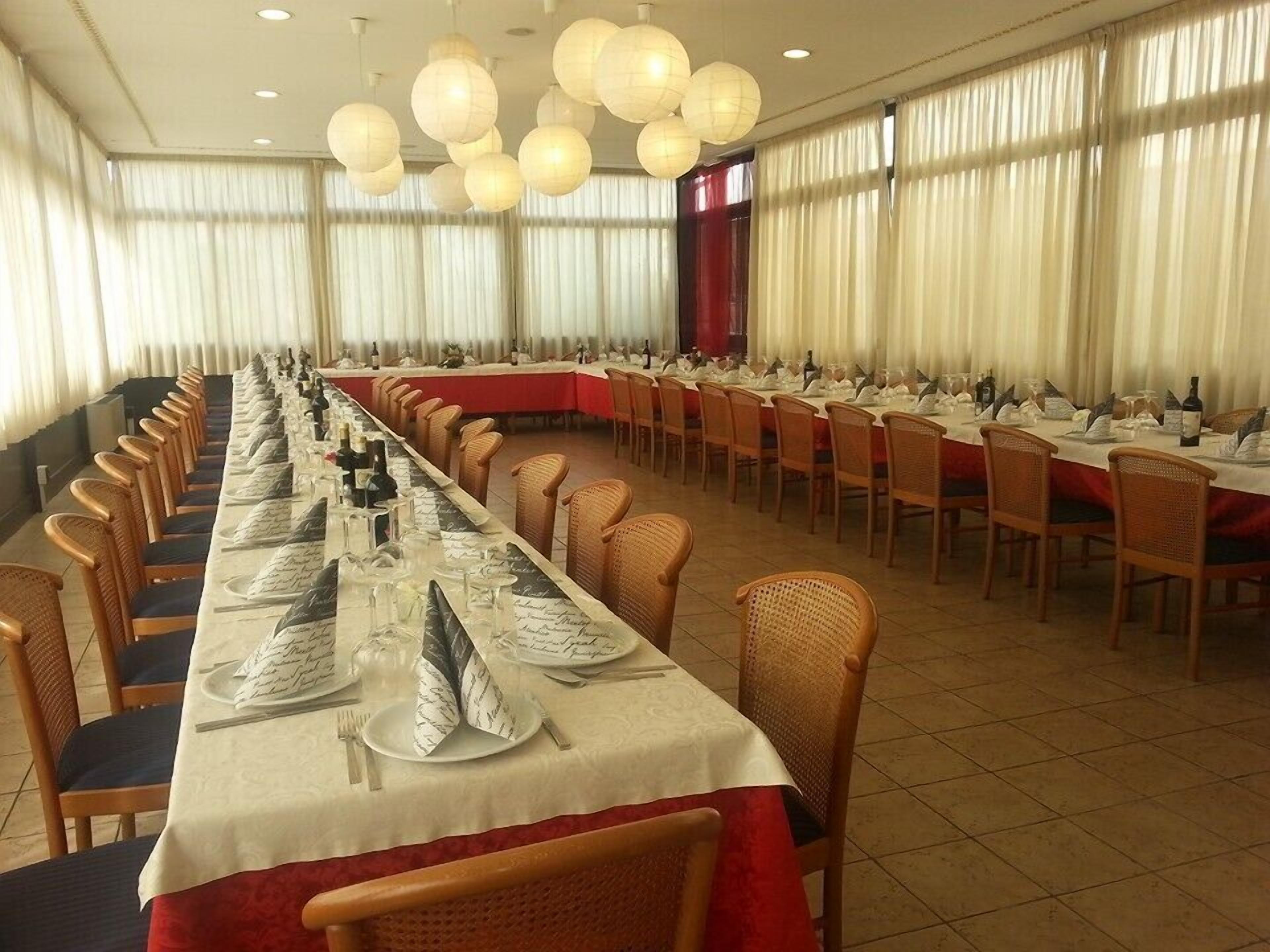 A banquet hall with long tables set for dining, wicker chairs, and hanging paper lanterns.
