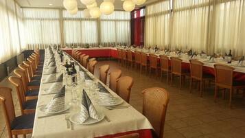 A banquet hall with long tables set for dining, wicker chairs, and hanging paper lanterns.