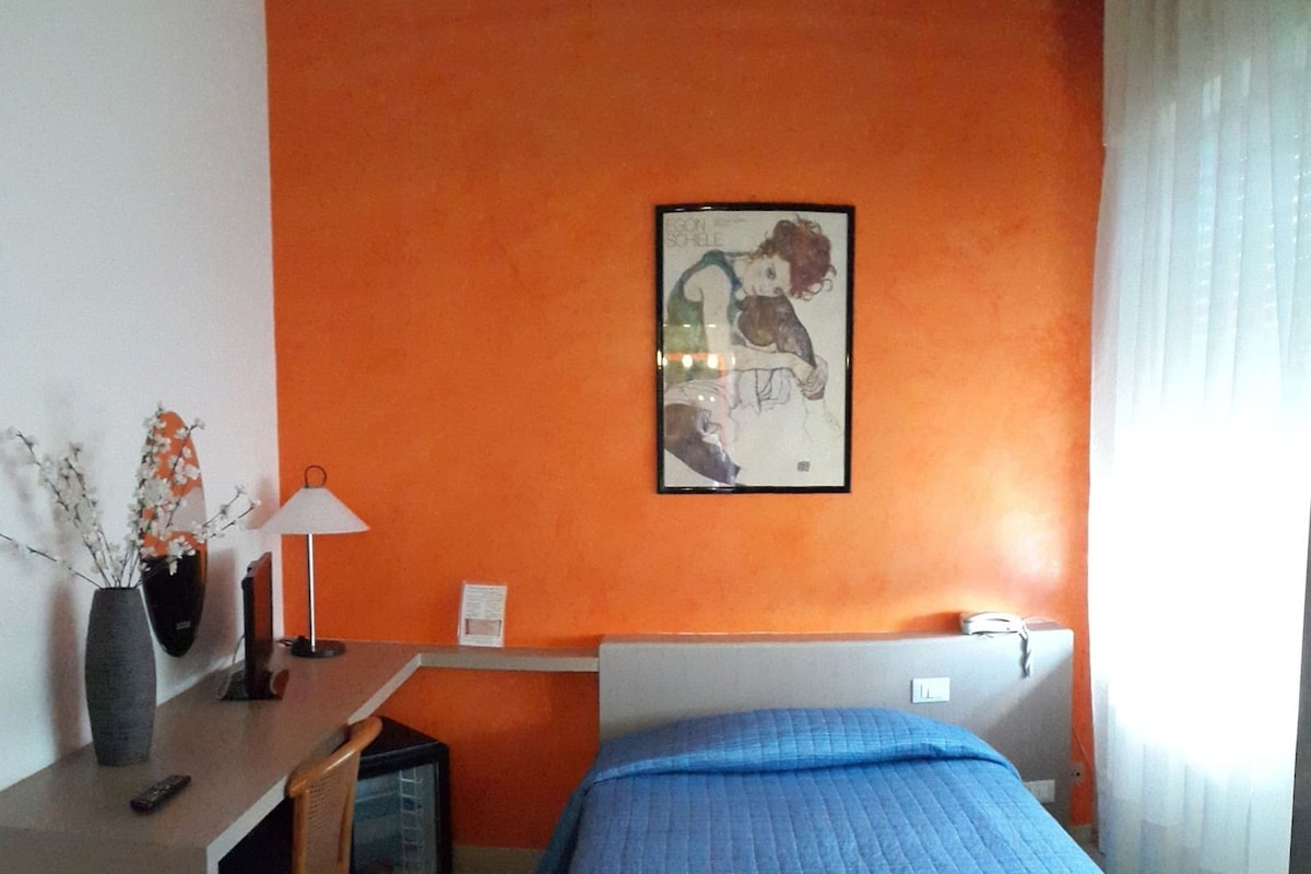 A room with a bed, a desk, a lamp, and a framed picture on the wall.