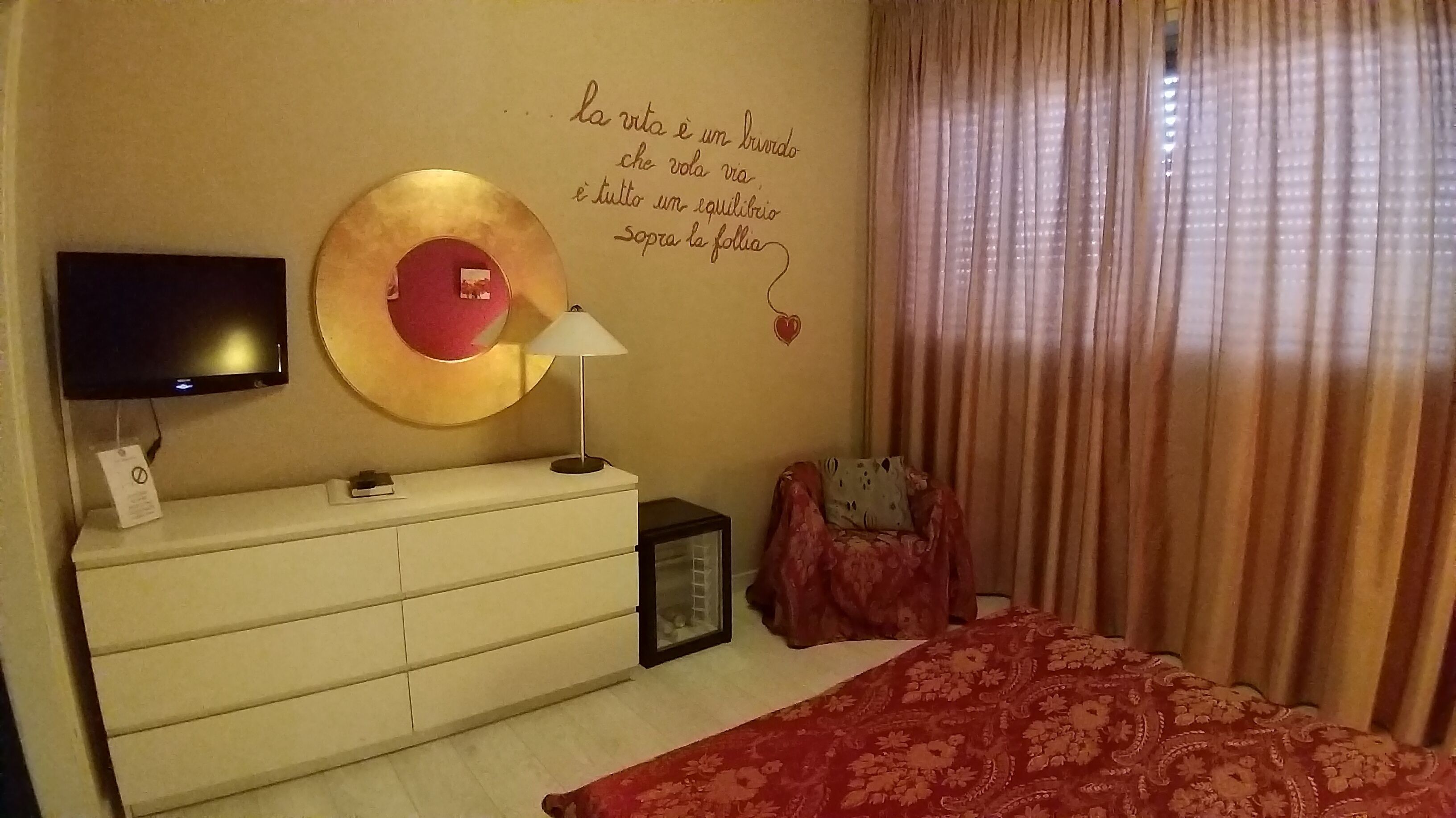 A bedroom with a bed, a dresser, a TV, and a wall with a quote.