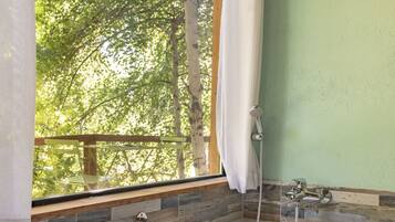 Un baño con bañera, una ventana con vistas a árboles y un cabezal de ducha.