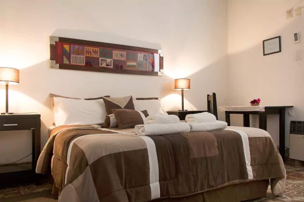 Ein Hotelzimmer mit Bett, zwei Nachttischen, einer Ablage, einem Wandbild und einem kleinen Tisch mit Lampe.