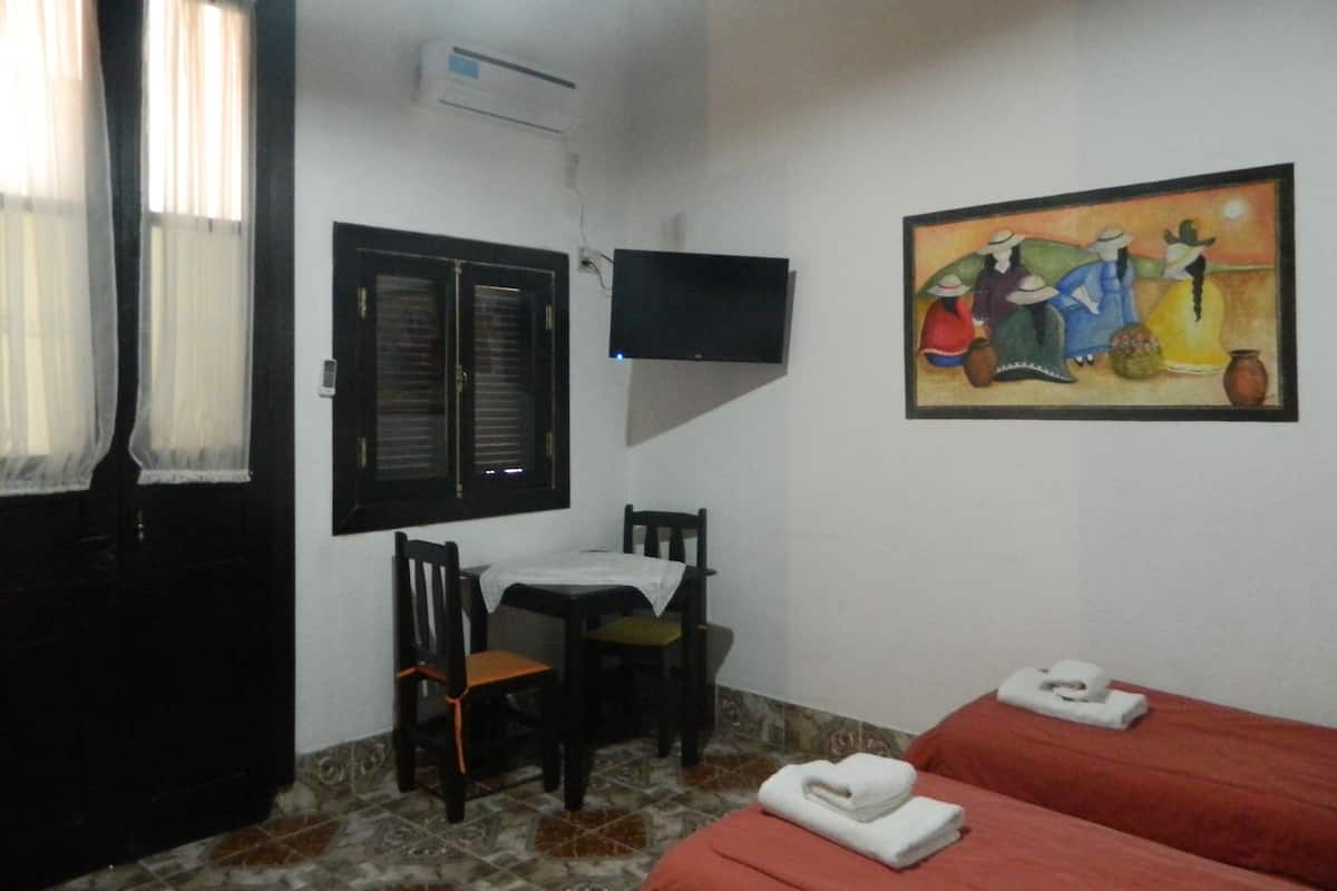 Ein Zimmer mit einem Bett, einem Sessel, einem Tisch, einem an der Wand befestigten Fernseher und einem Gemälde.