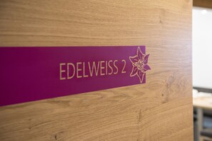 A wooden panel with the text "EDELWEISS 2" and a purple floral logo. - smartFLATS (Dorfgastein)