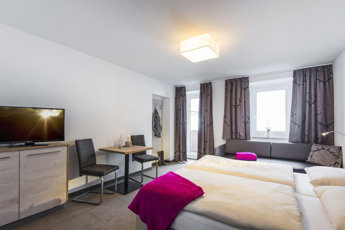 Quarto de hotel com cama, escrivaninha, cadeira, televisão e cortinas.