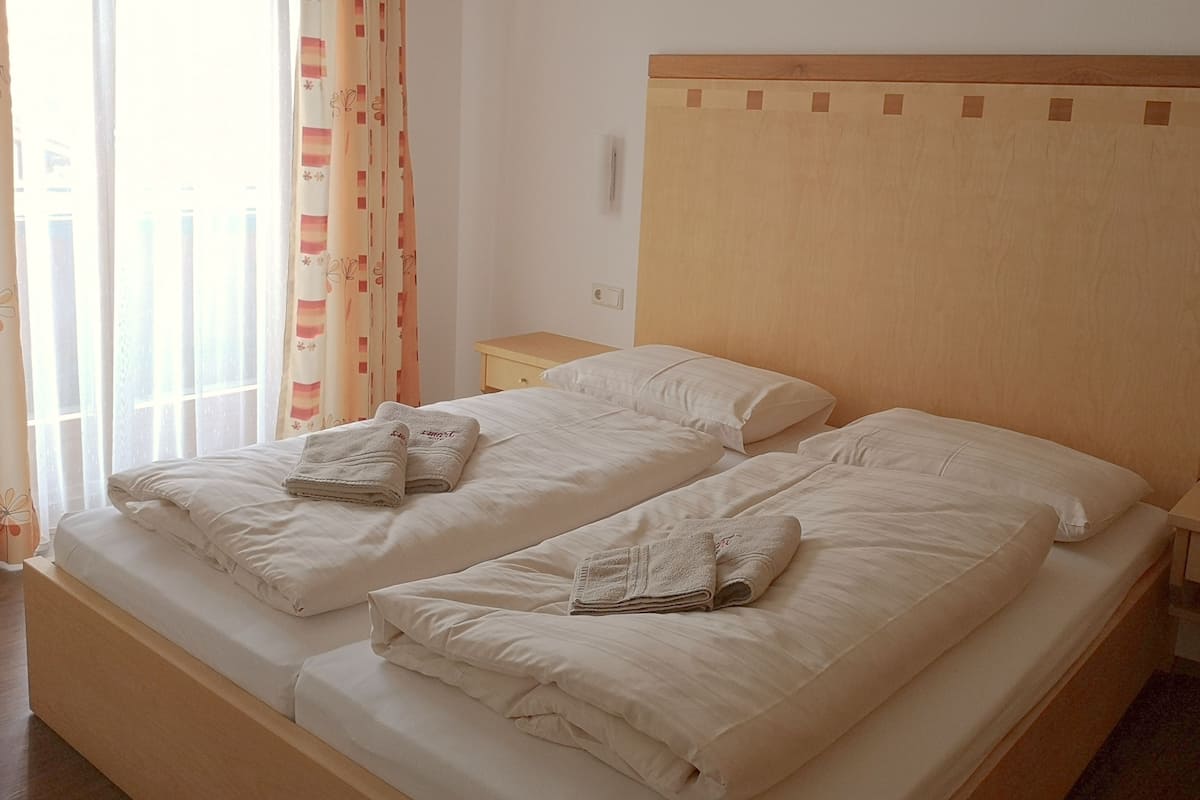 Uma cama de casal com lençóis brancos e duas toalhas dobradas.