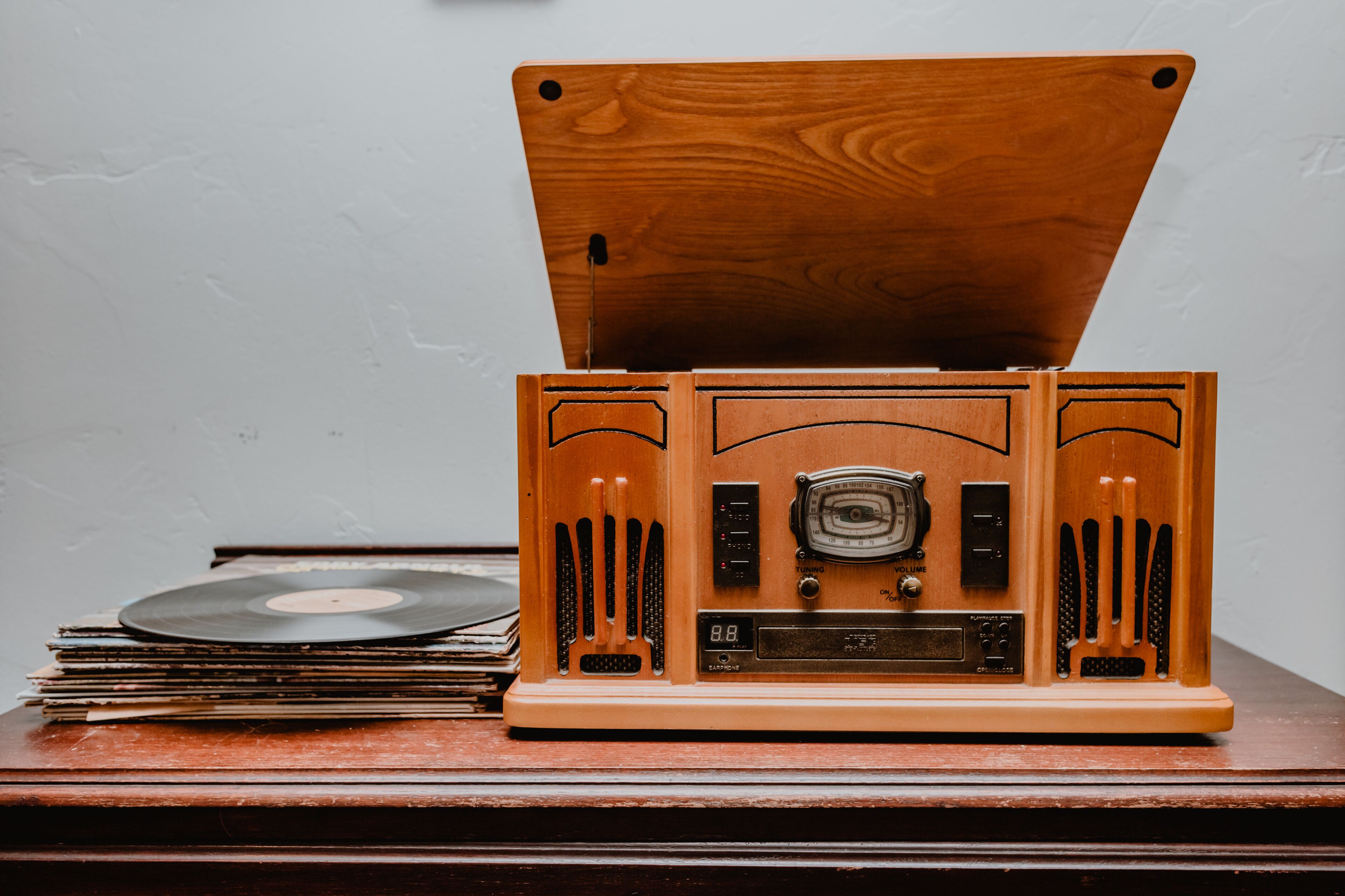 A vintage record player with a wooden top and front panel, placed on a wooden surface with vinyl records and a stack of books beside it.