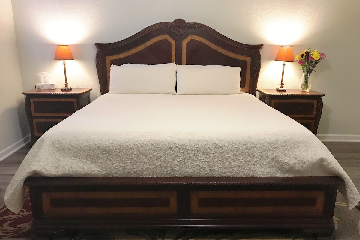 A large bed with a wooden headboard, two bedside tables with lamps, and a floral arrangement on one table.