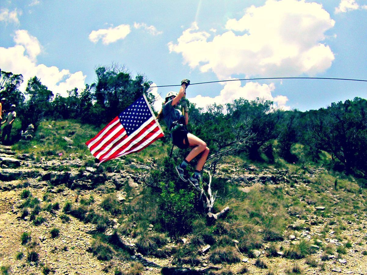 A person on a rope swing holding an American flag.