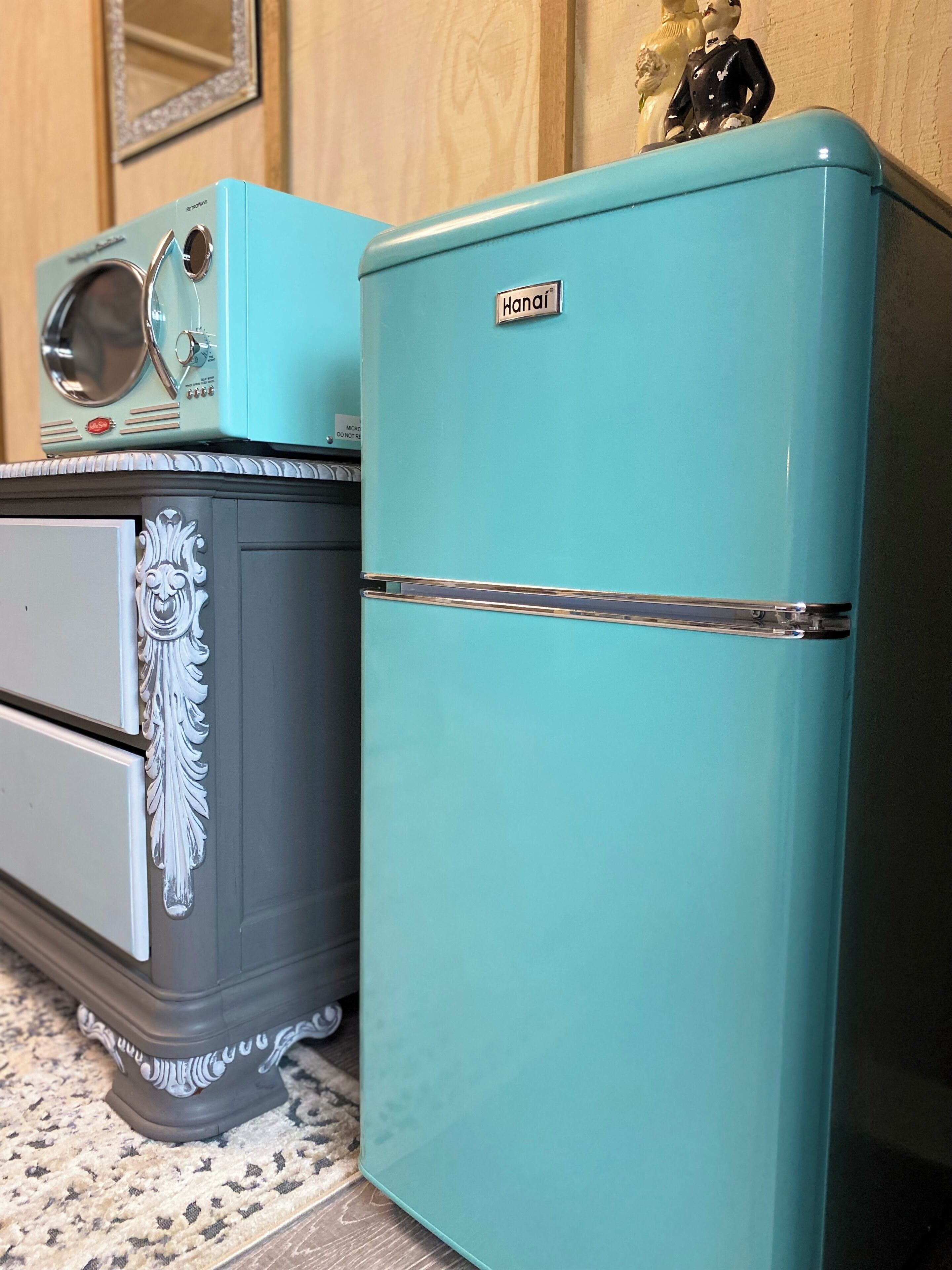 Two vintage refrigerators, one teal and one light blue, with decorative patterns and a brand name visible.