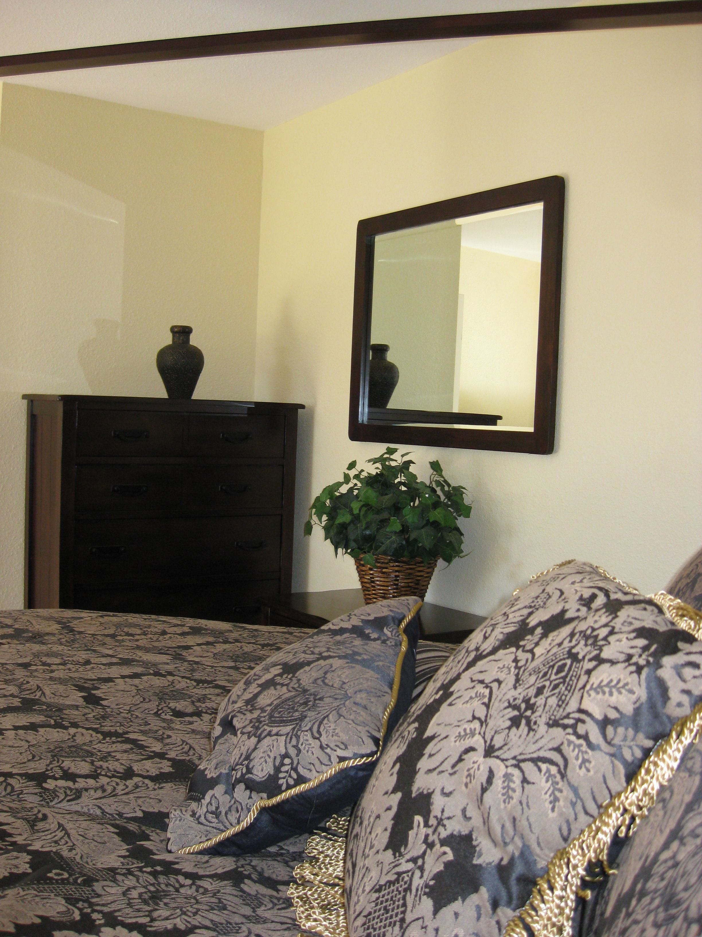 A bedroom with a bed, a dresser, a mirror, and a potted plant.