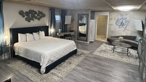 A bedroom with a large bed, a desk, a chair, a sofa, and a coffee table. - Square Inn (Wimberley)