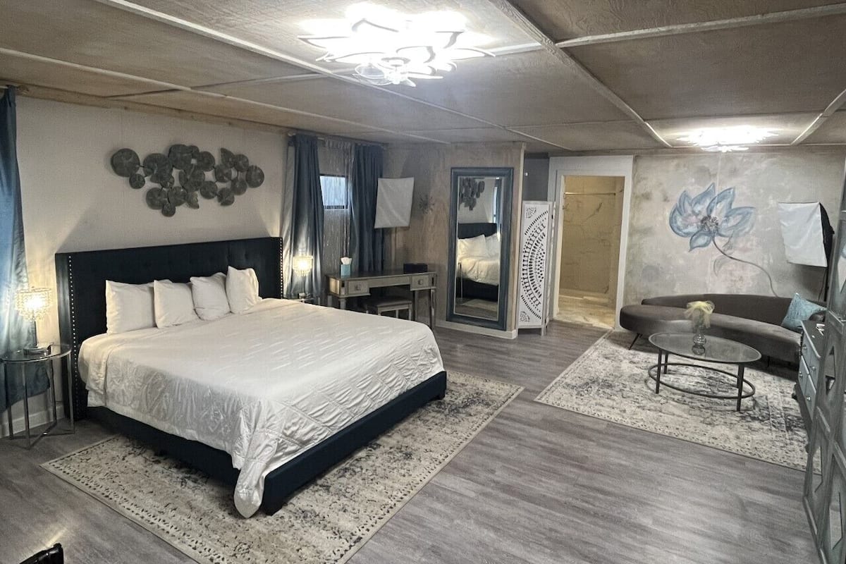 A bedroom with a large bed, a desk, a chair, a sofa, and a coffee table.