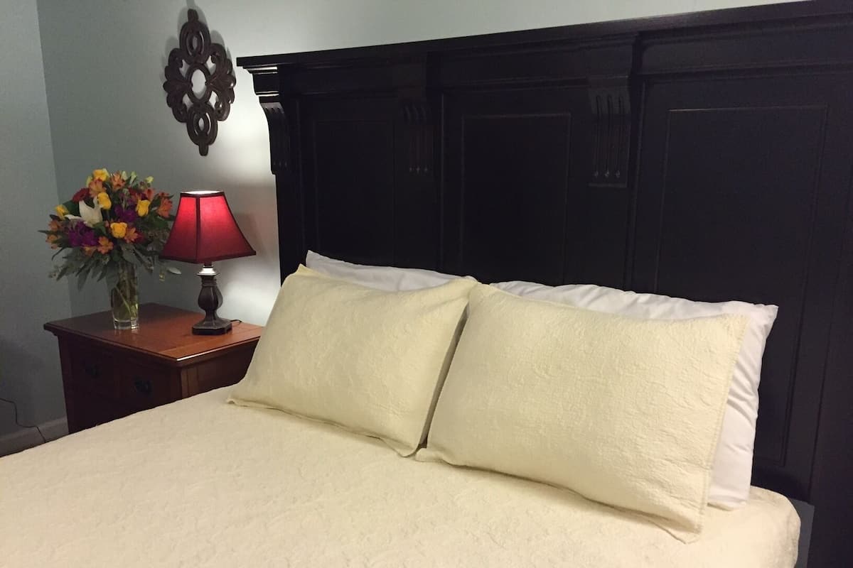 A neatly made bed with two pillows, a bedside table with a lamp and a vase of flowers.