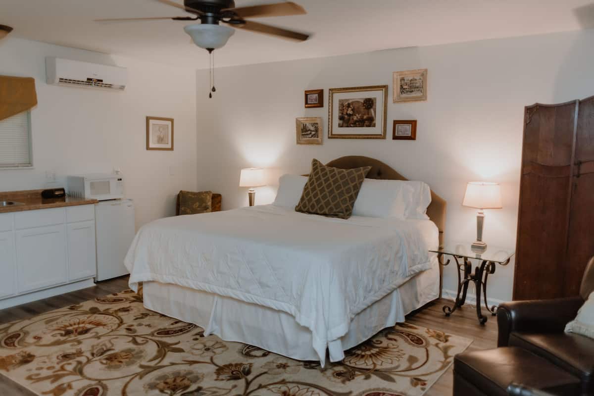 A bedroom with a bed, two bedside lamps, a ceiling fan, a wooden door, and a small table with a lamp.