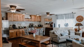 A spacious kitchen with wooden cabinets, a dining area with a wooden table, and a living room with a sofa and a coffee table. - Square Inn (Wimberley)