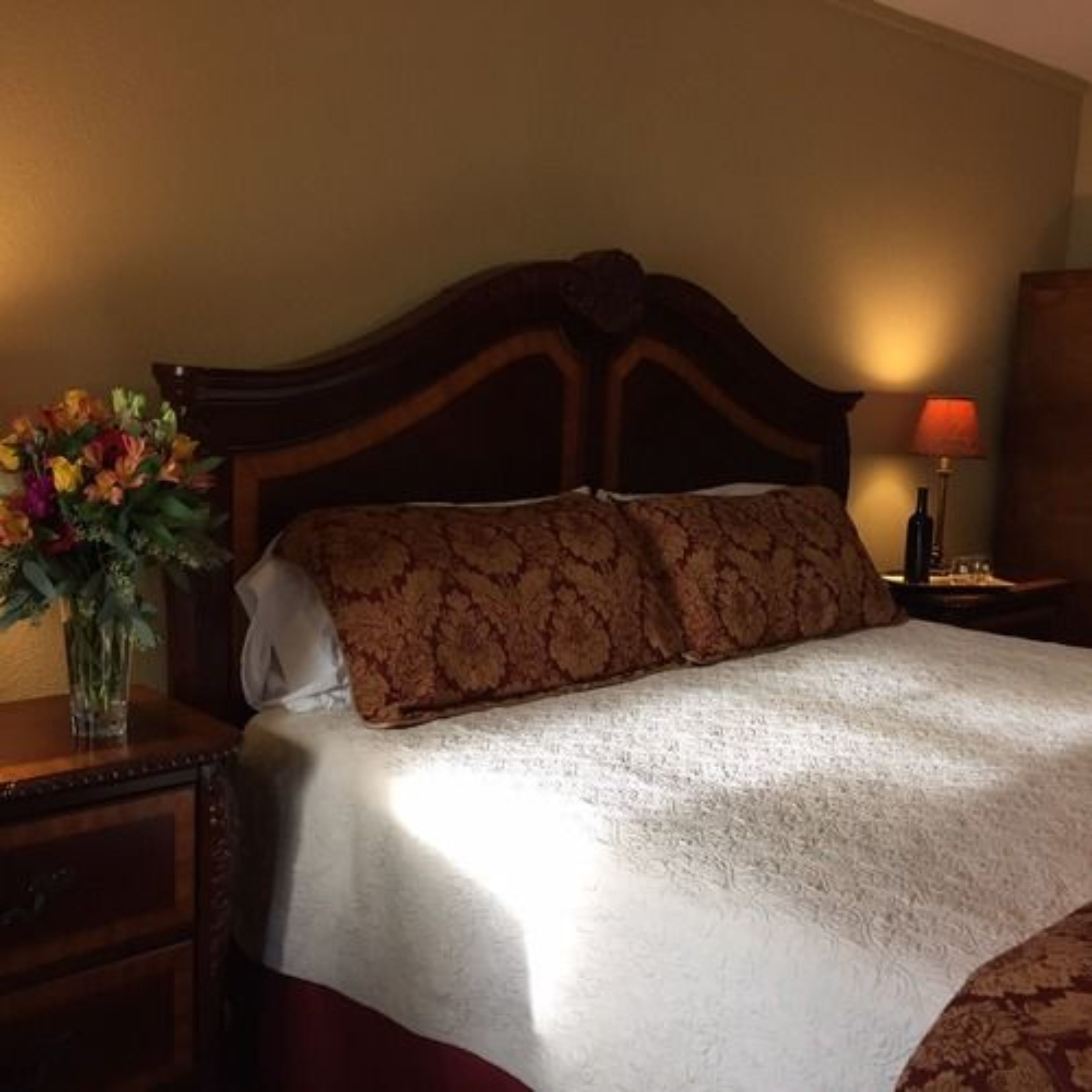 Una cama bien tendida con un cabecero estampado, una mesita de noche con un florero y una lámpara en la mesilla.