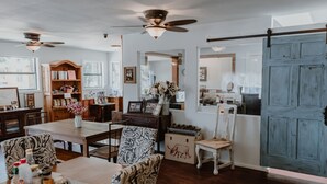 A dining area with wooden furniture, a ceiling fan, and a large blue door. - Square Inn (Wimberley)