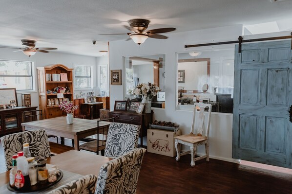 A dining area with wooden furniture, a ceiling fan, and a large blue door. - Square Inn (Wimberley)