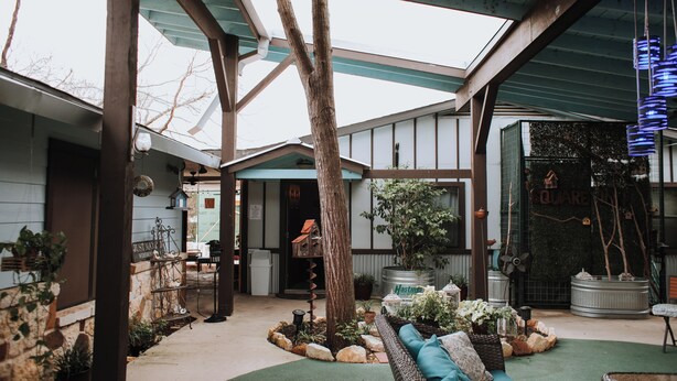 A covered outdoor patio with a seating area, a tree, and potted plants. - Square Inn (Wimberley)