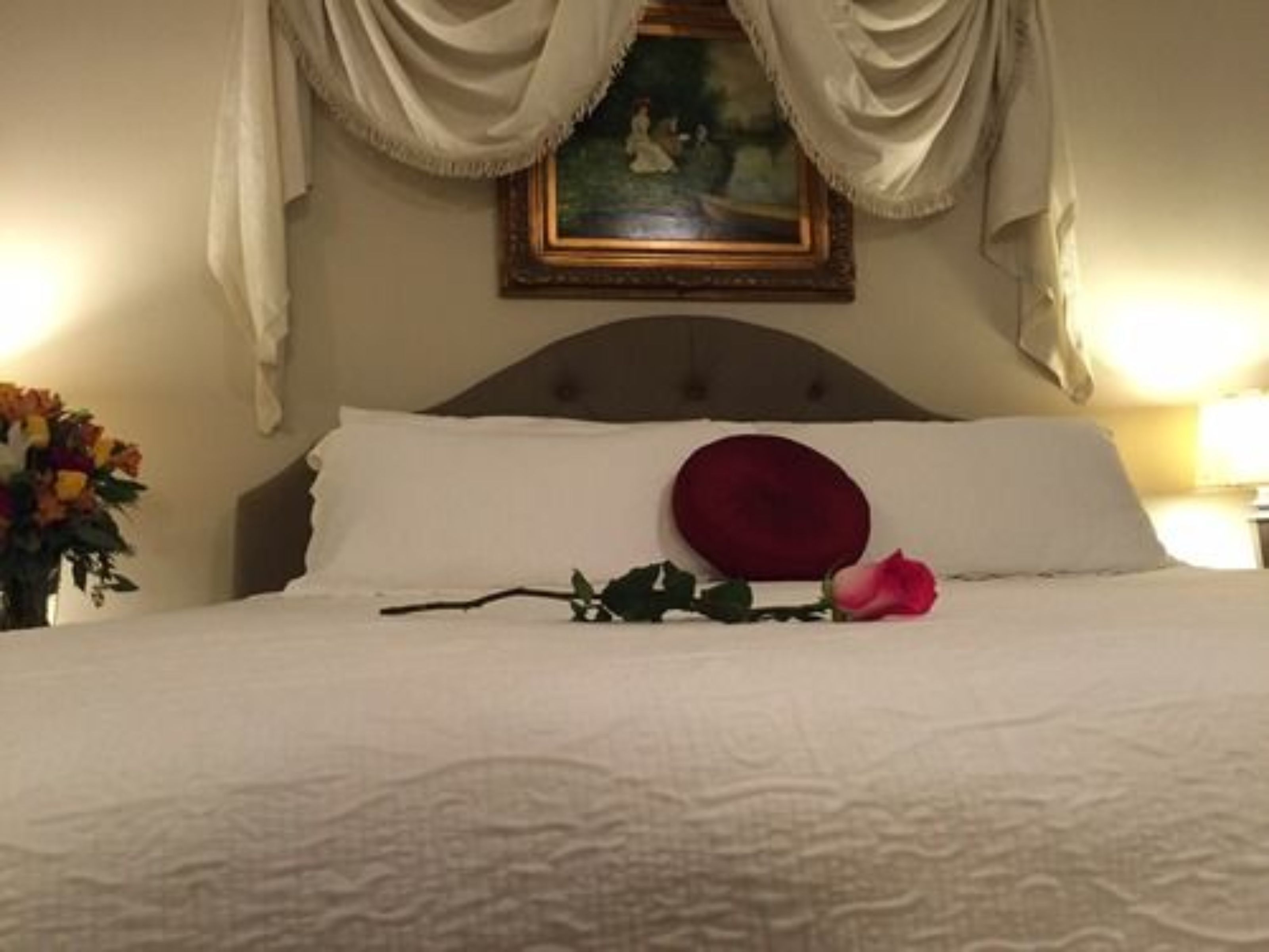 Un lit bien fait, avec des draps blancs, un seul oreiller rouge et une rose rose posée sur le lit.