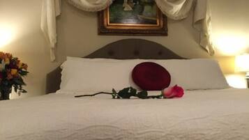 Un lit bien fait, avec des draps blancs, un seul oreiller rouge et une rose rose posée sur le lit.