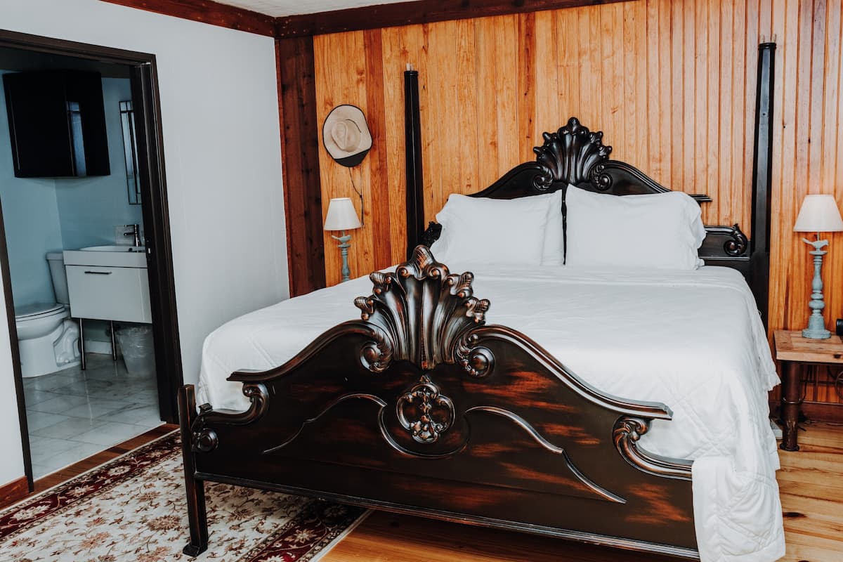 A wooden-paneled bedroom with a large bed, a bedside table with a lamp, and a wooden floor.