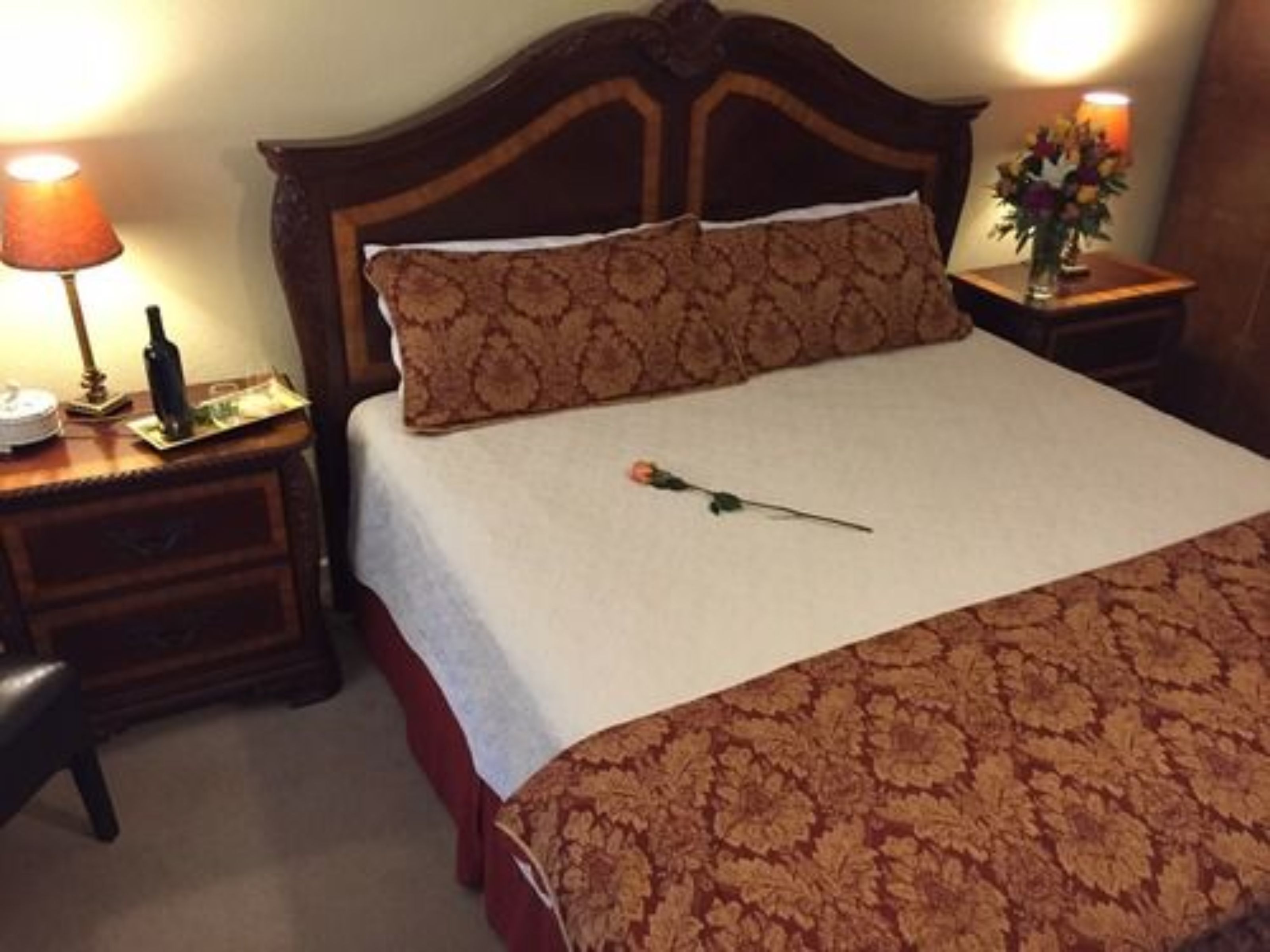 Una cama bien hecha con una colcha estampada y una sola rosa sobre la almohada.