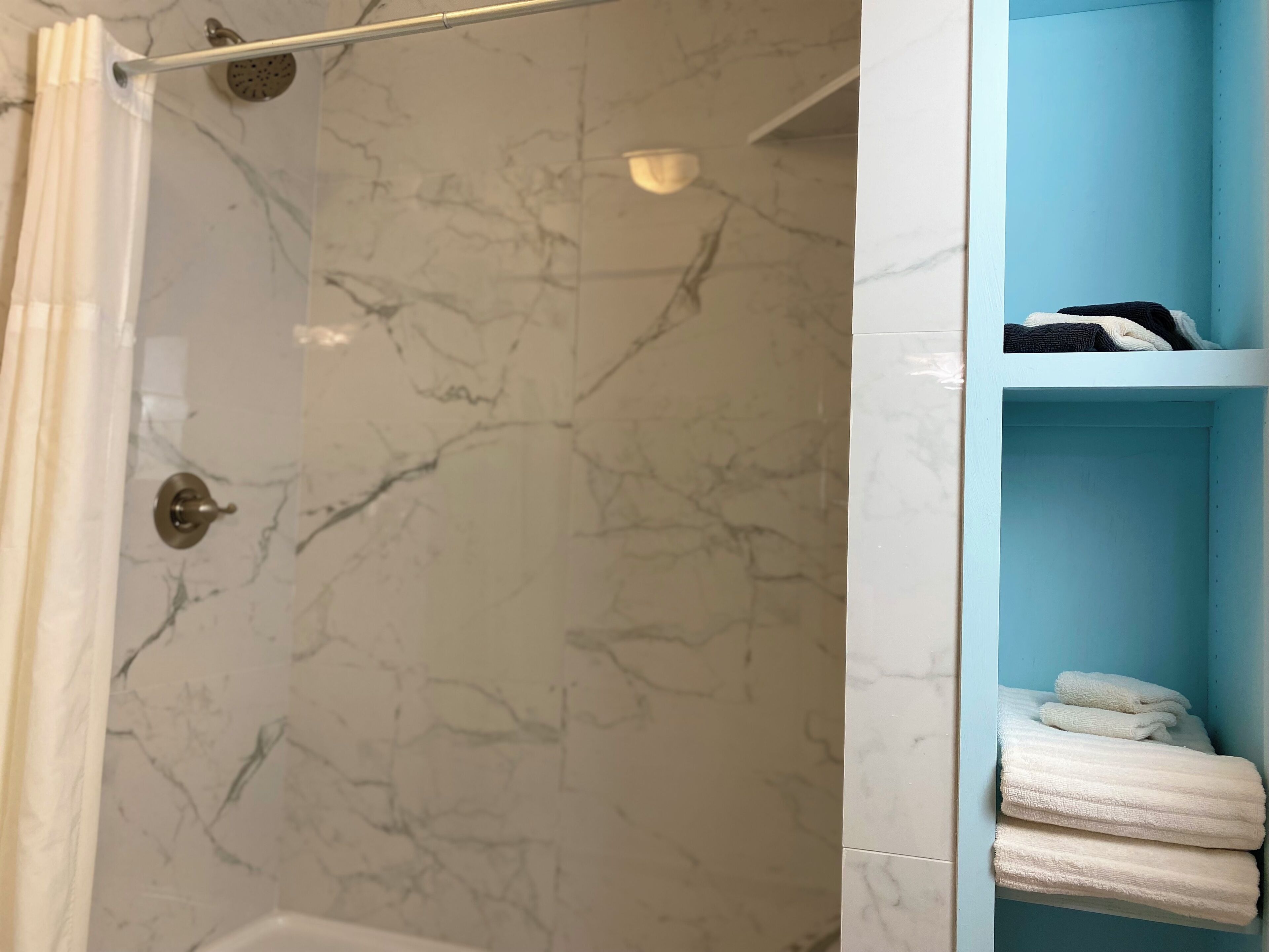 A bathroom with a shower area and a blue storage unit with towels.