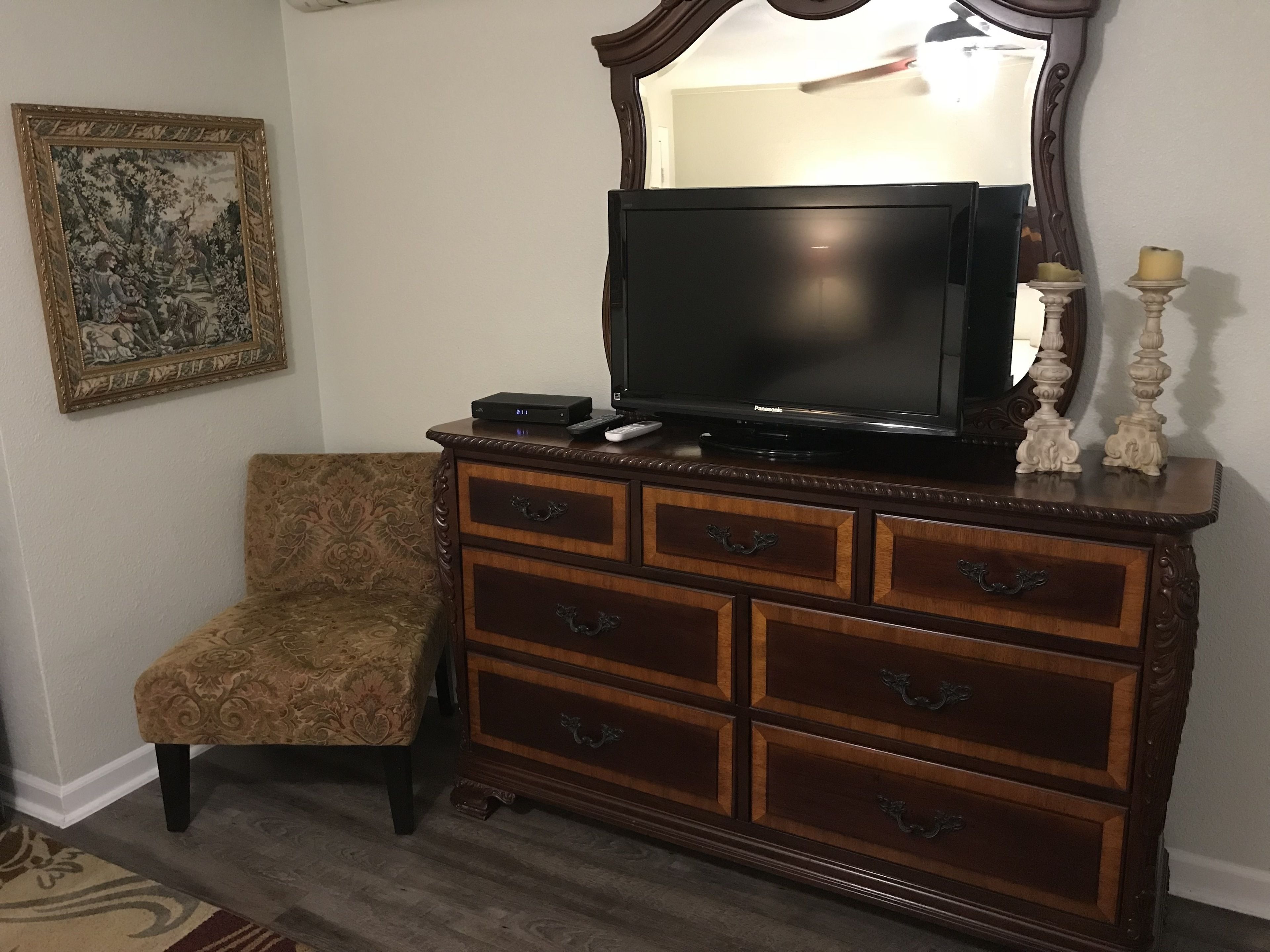 A wooden dresser with a flat-screen TV, a chair, and a framed picture on the wall.