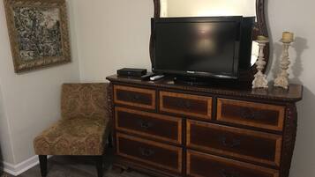 A wooden dresser with a flat-screen TV, a chair, and a framed picture on the wall.