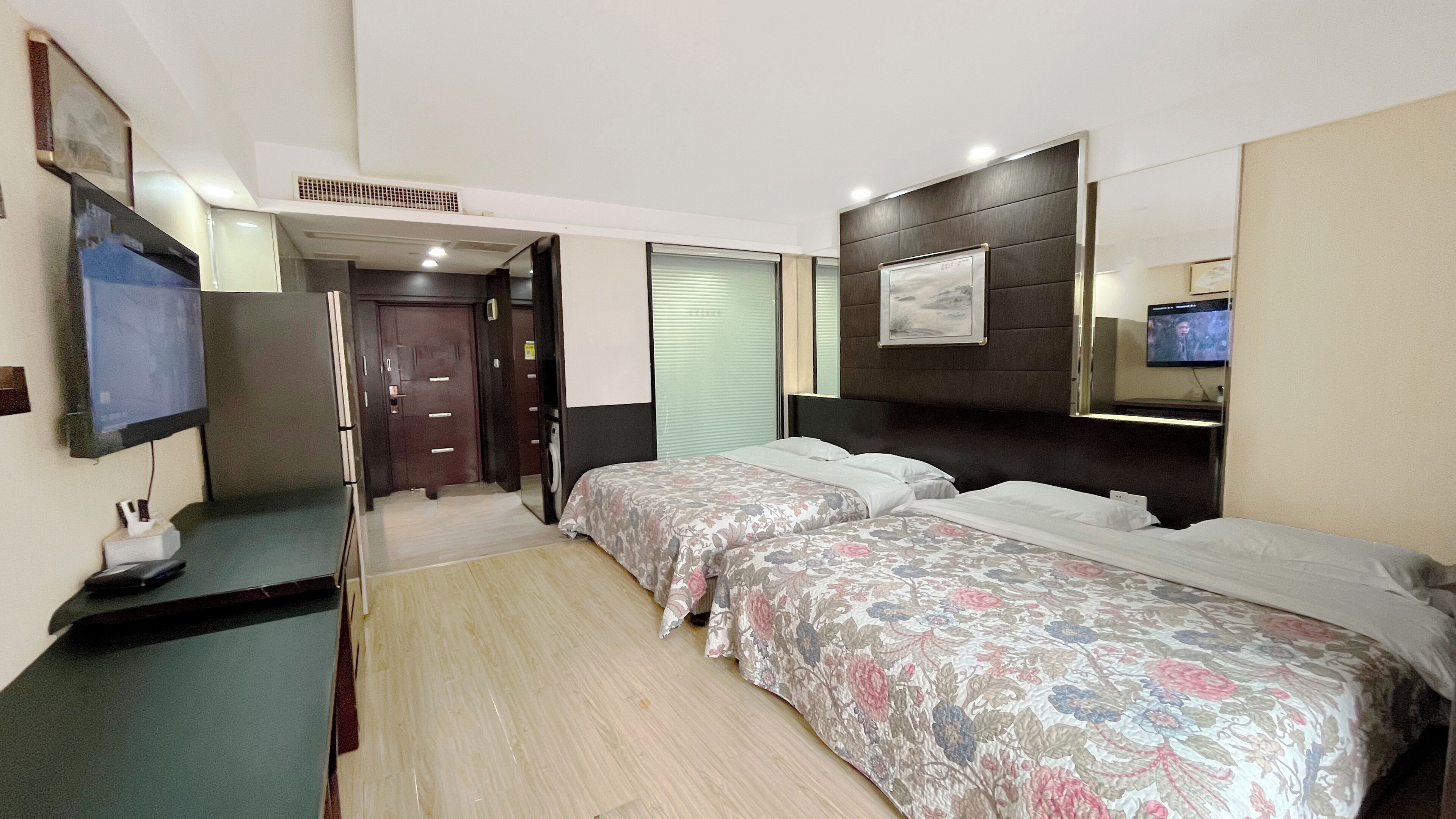 Ein Hotelzimmer mit zwei Betten, einem Fernseher, einem Schreibtisch und einem Spiegel.