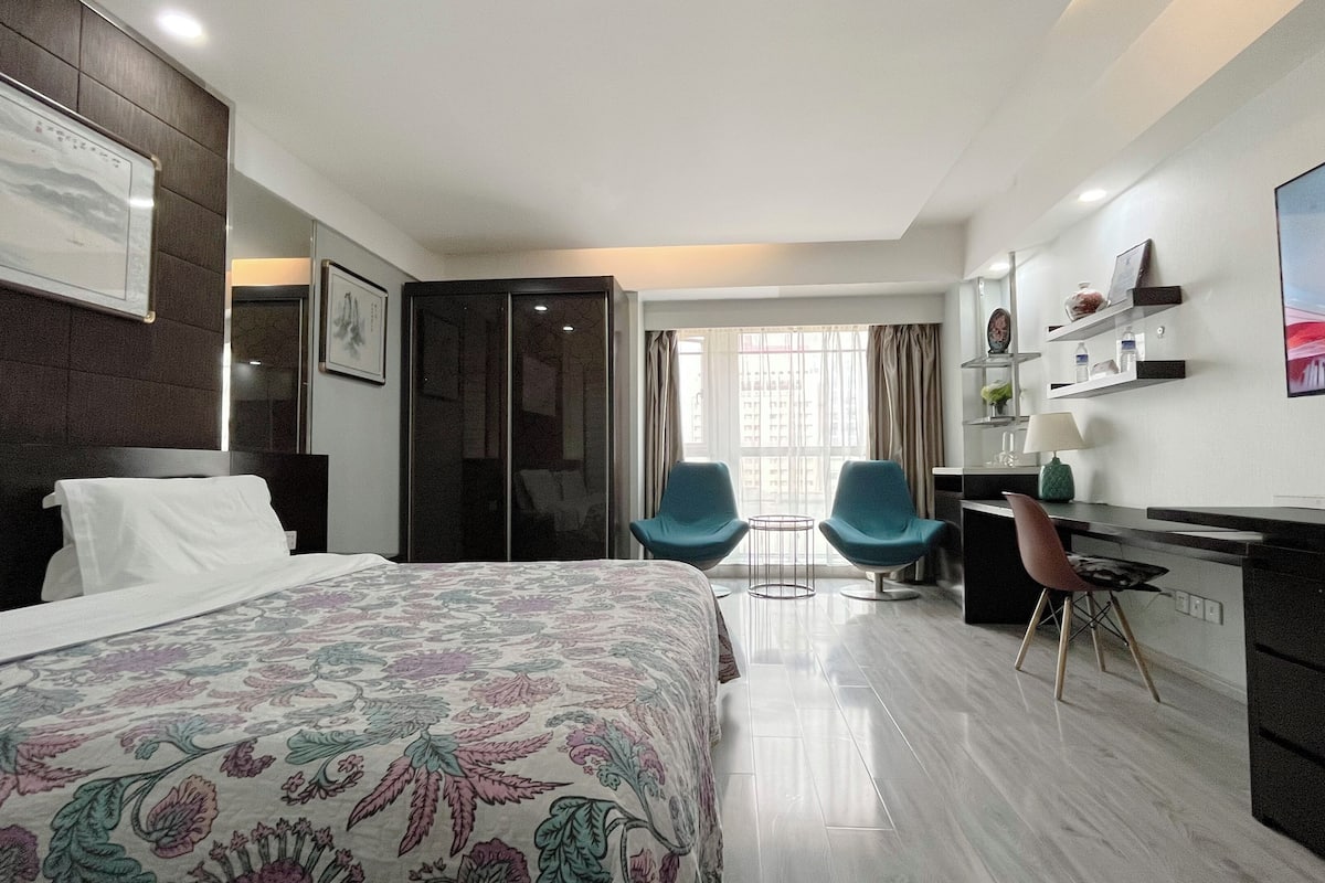 Une chambre d’hôtel moderne avec un grand lit, deux fauteuils, un bureau et une télévision.