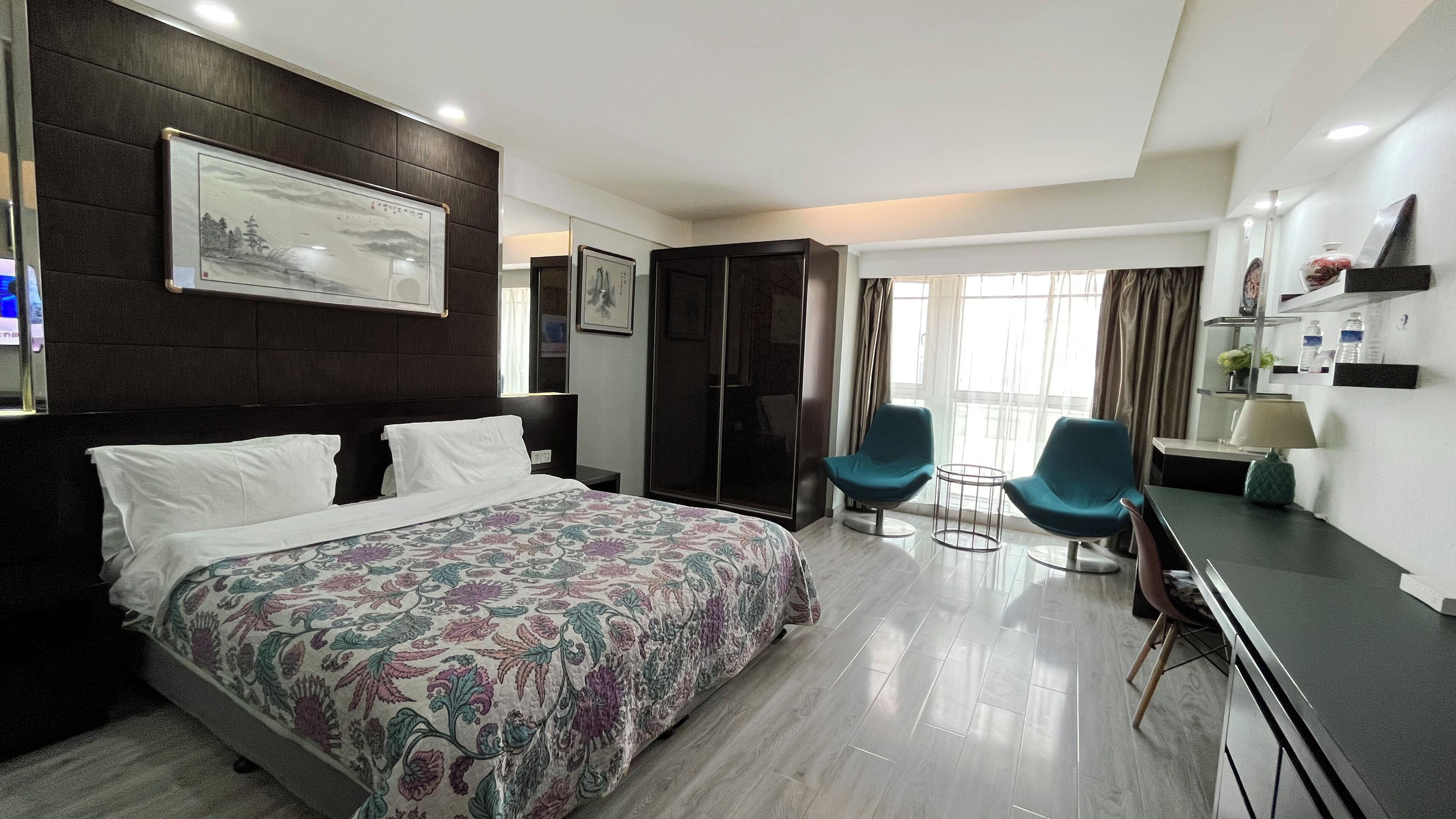 A hotel room with a large bed, two chairs, a desk, a wardrobe, and a window with curtains.
