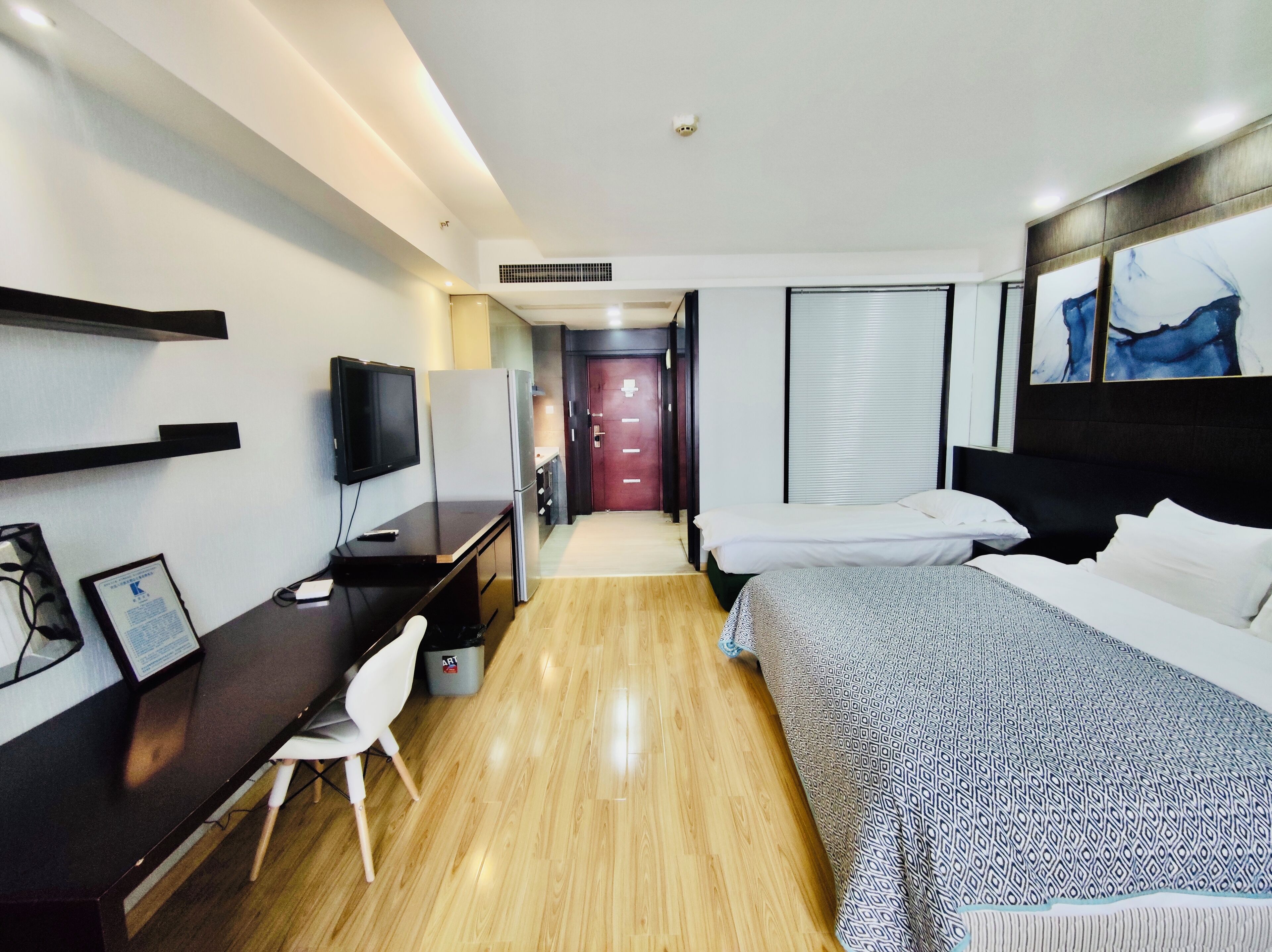 A hotel room with a bed, a desk with a chair, a television, and a door leading to another room.