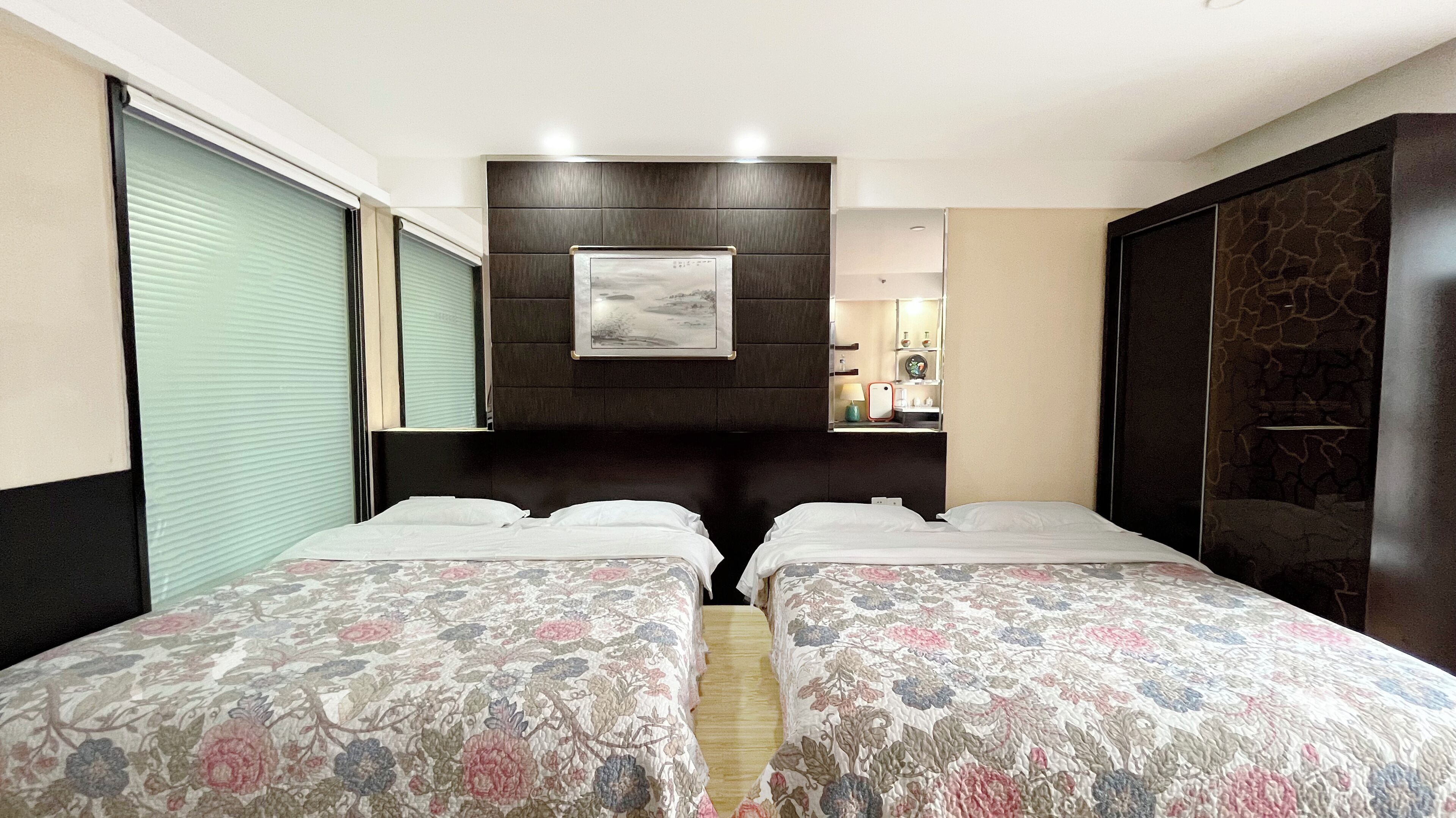 A hotel room with two beds, a dark headboard, a framed picture, and a small bedside table with a lamp.