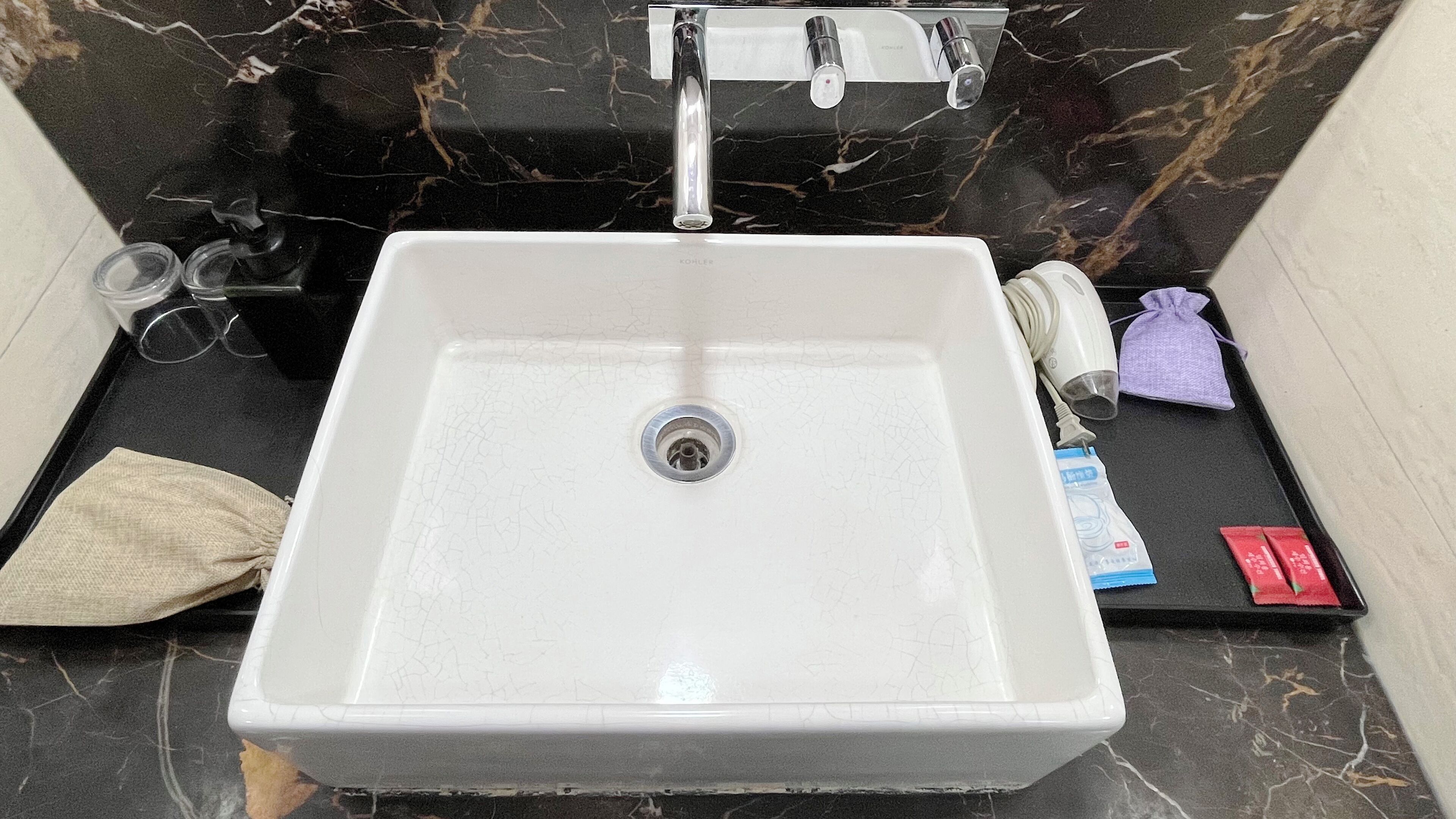 Un bagno con un lavandino bianco, una schiena di marmo nero e un asciugamano sul pavimento.
