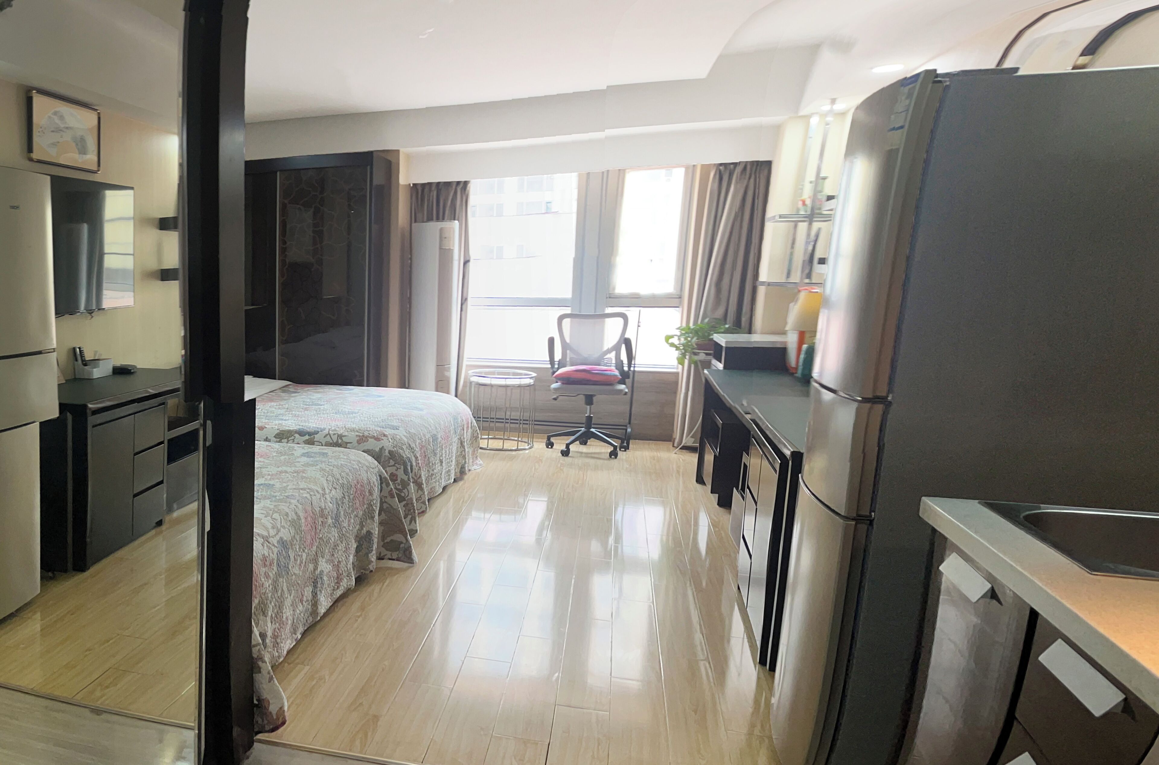 A hotel room with a bed, a desk, a chair, a refrigerator, and a window with curtains.