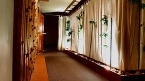 A corridor with a wooden floor, beige curtains, and bamboo plants in a planter. - Holiday Spa Hotel (Cebu City)
