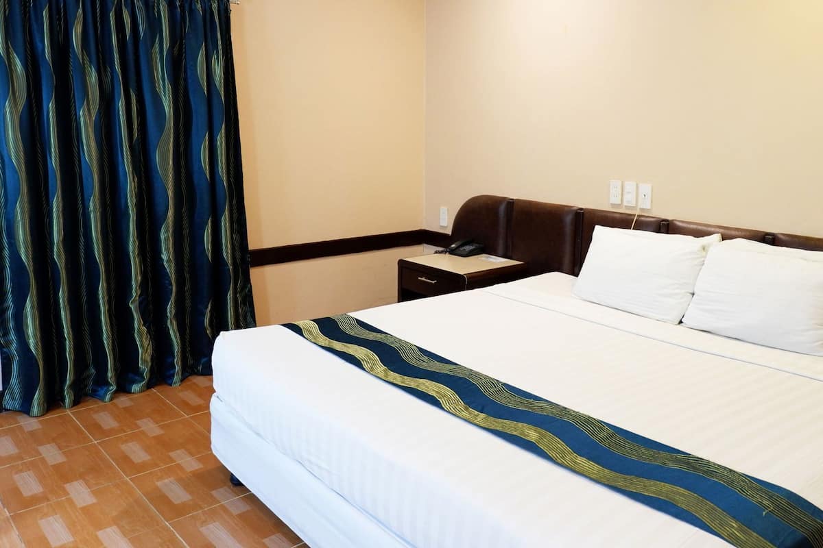 Hotellihuone, jossa on sänky, yöpöytä, puhelin ja verho.