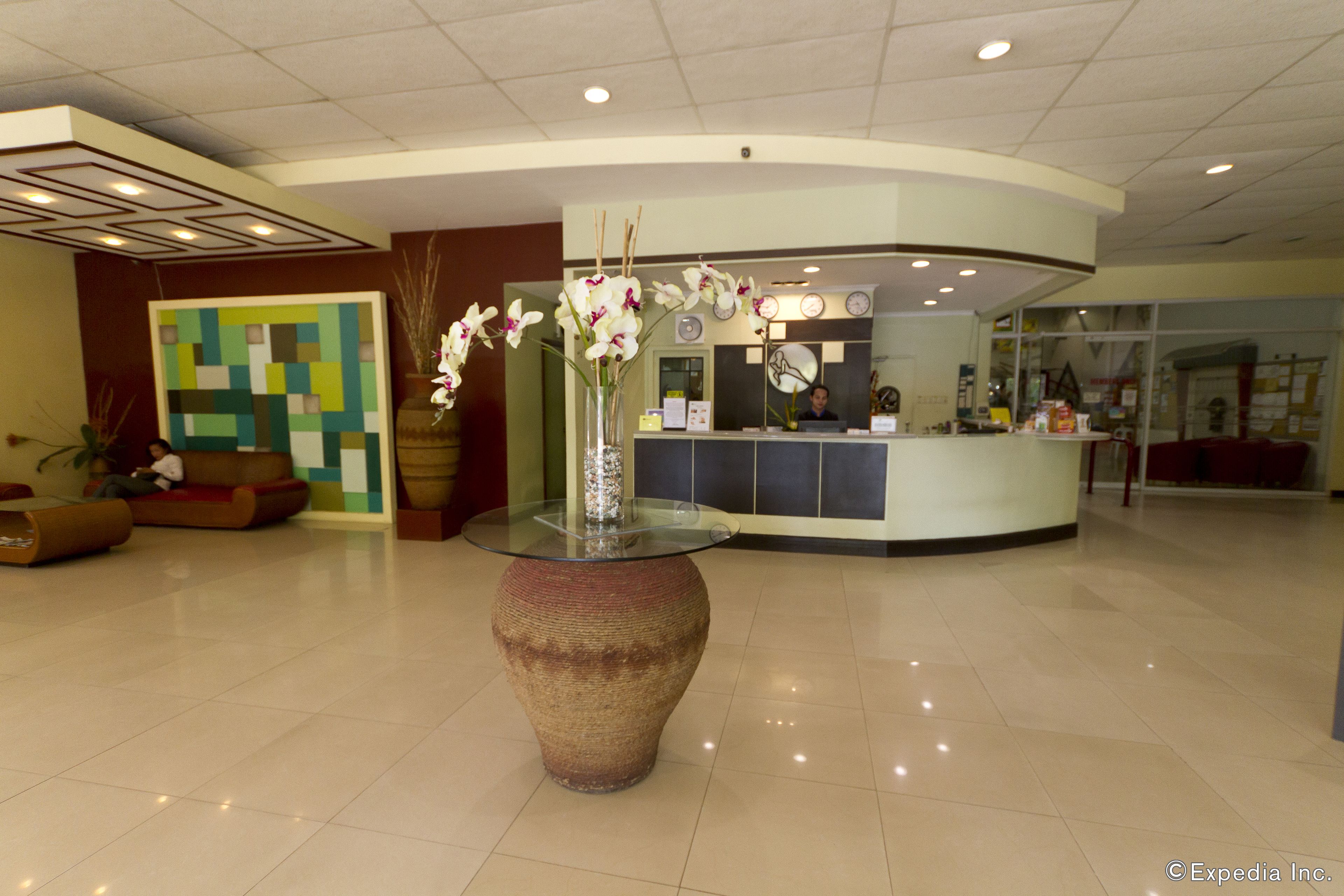 A reception area with a glass-top table, a large vase with flowers, a reception desk, and a colorful wall art piece.