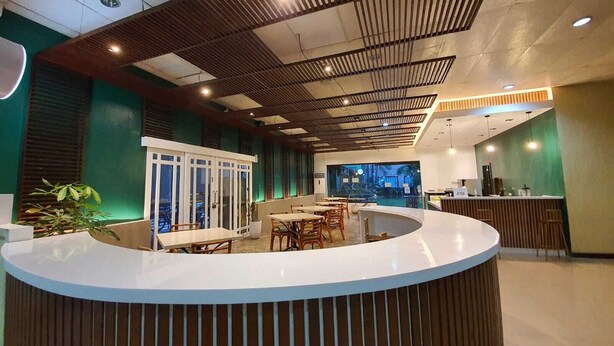 A modern reception area with a curved counter, wooden slatted ceiling, and a view of a pool and outdoor area. - Holiday Spa Hotel (Cebu City)